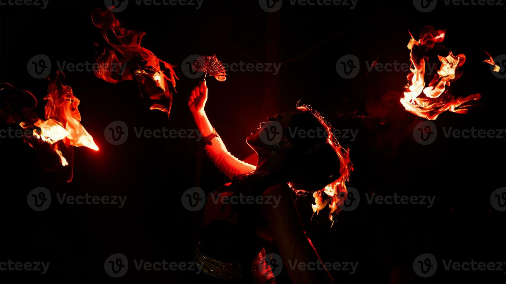 The silhouette of a female dancer holding jewelry in the dark of night is lit by the light of a burning fire photo