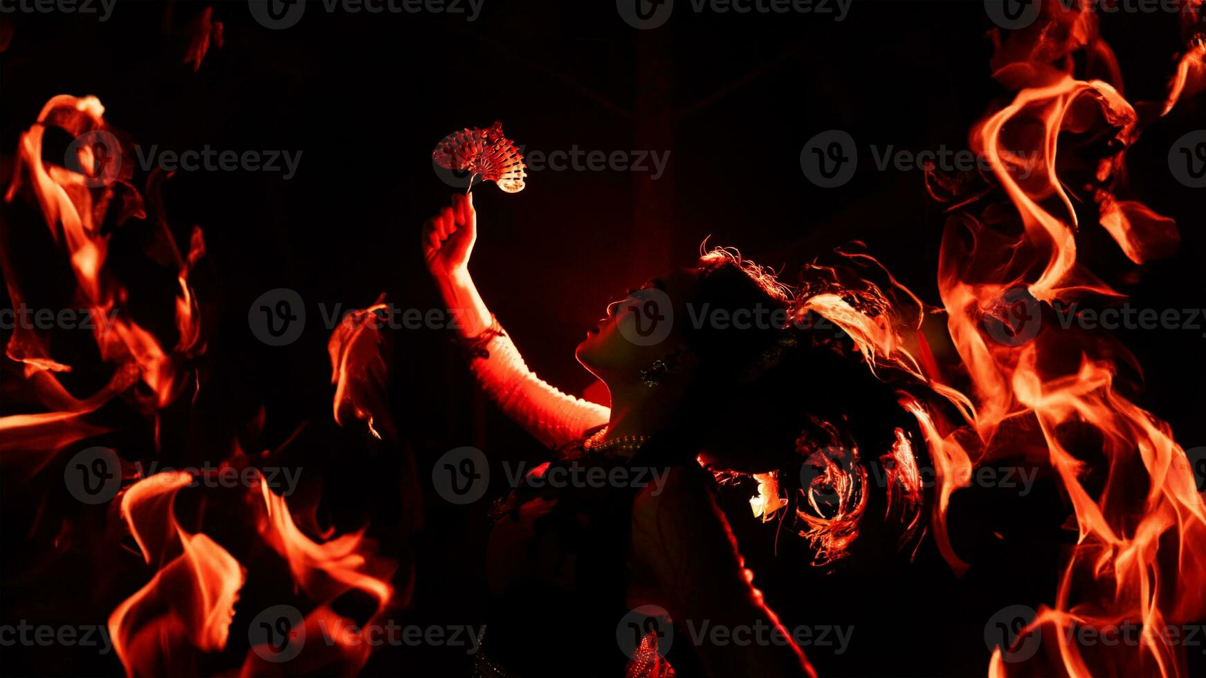 the silhouette of a female dancer holding jewelry shines brightly around the flames and looks bold in the dark photo