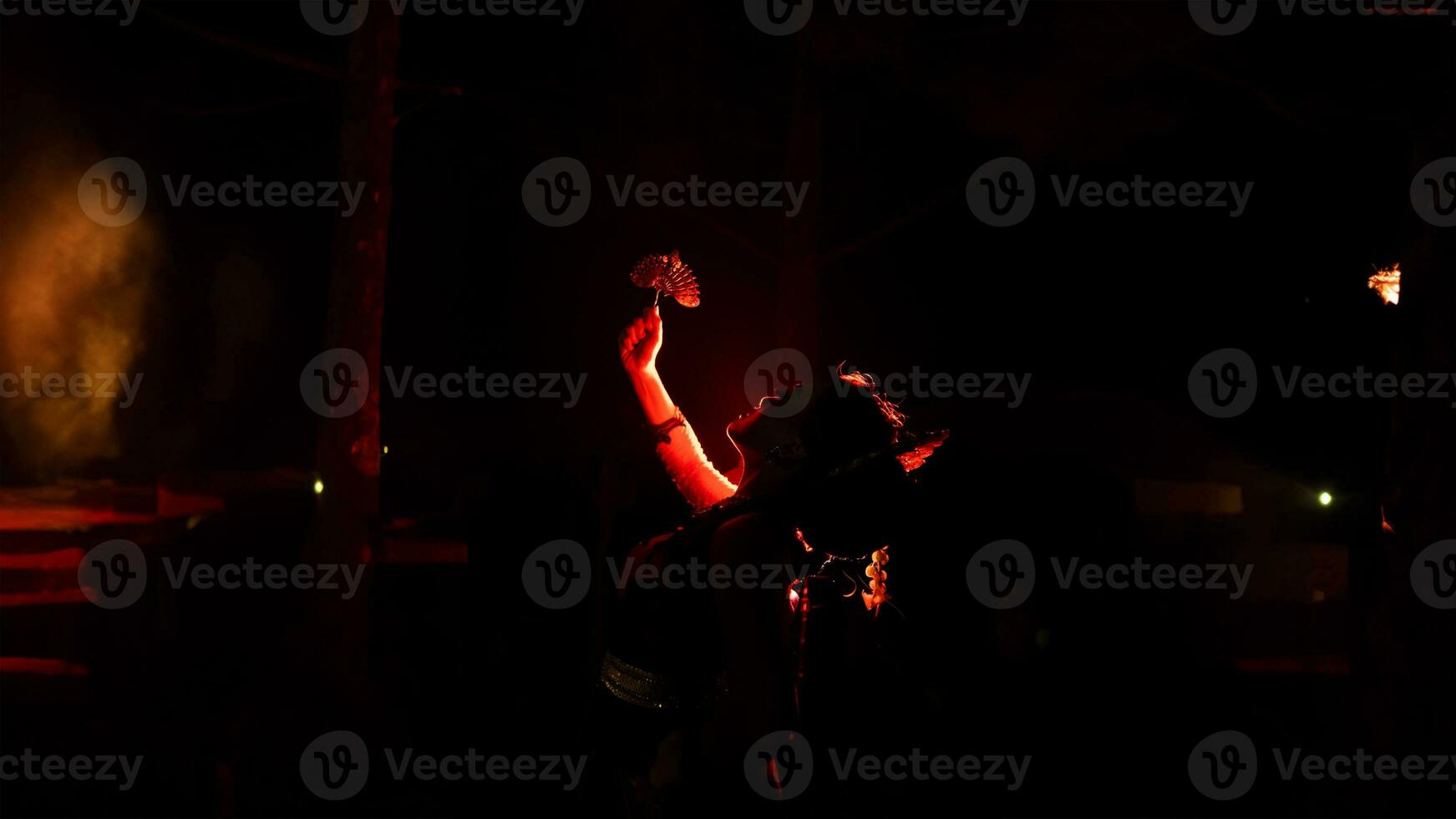 The silhouette of a female dancer holding jewelry in the dark of night is lit by the light of a burning fire photo