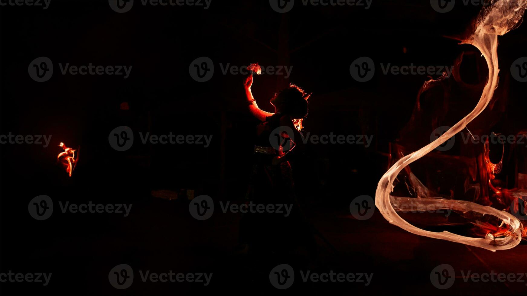 the silhouette of a female dancer holding jewelry shines brightly around the flames and looks bold in the dark photo