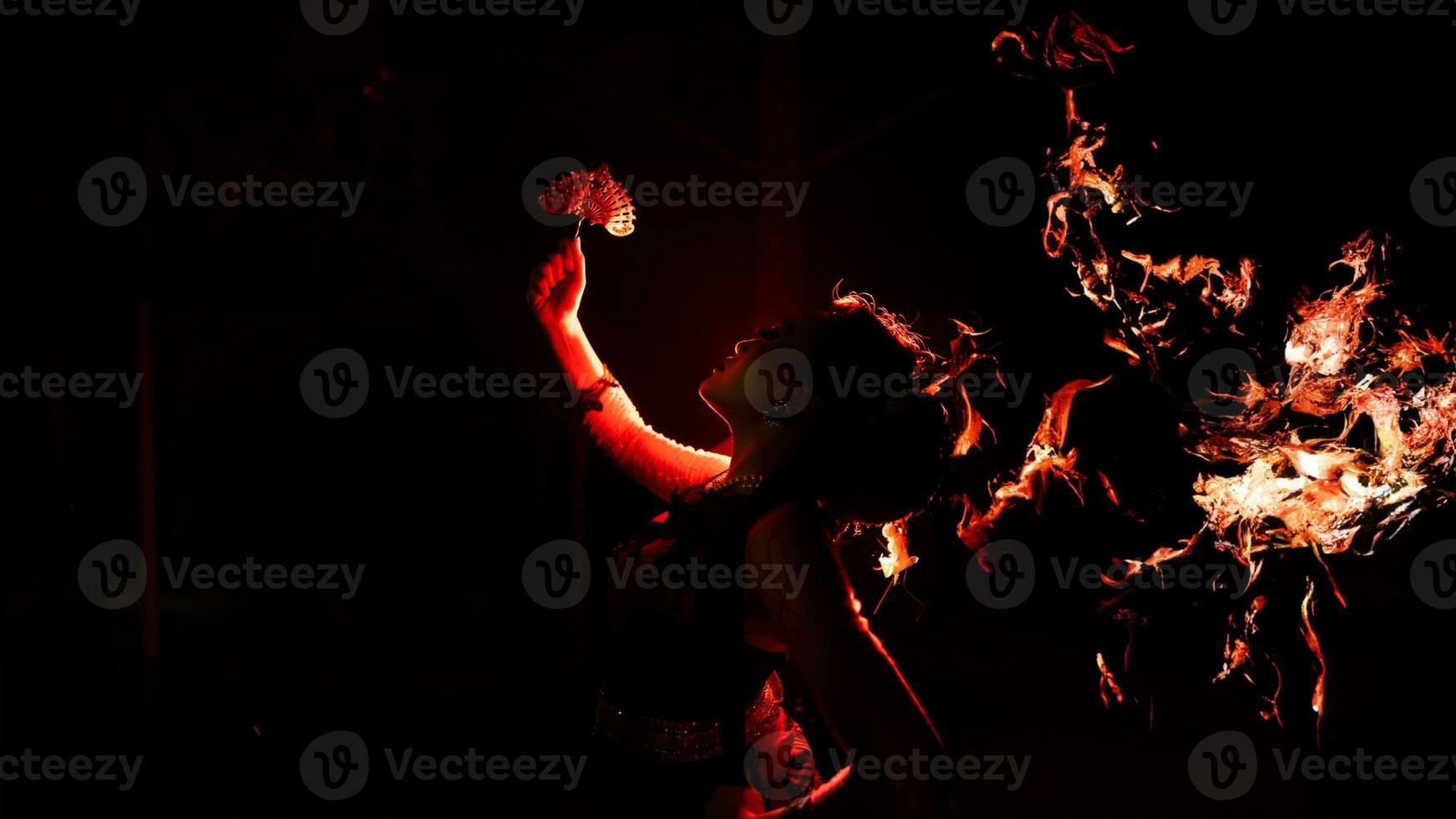 the silhouette of a female dancer holding sparkling jewelry and looking sharp in the dark with fire burning in the background photo