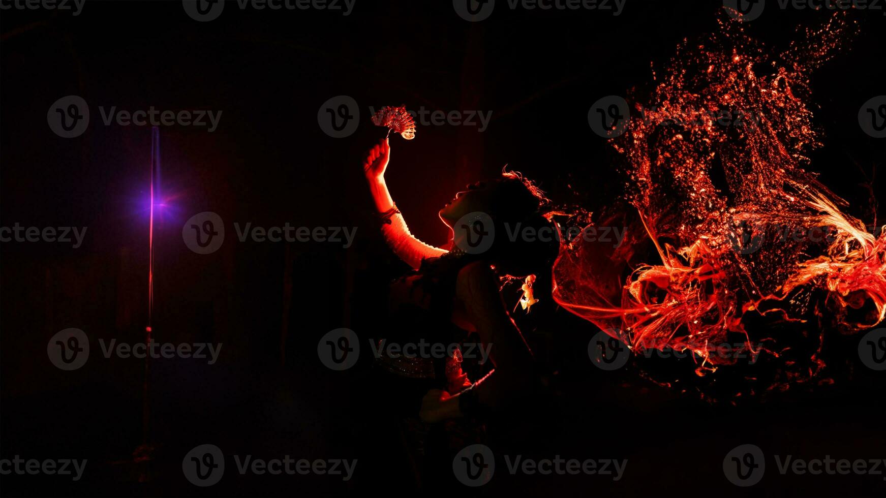 the silhouette of a female dancer holding sparkling jewelry and looking sharp in the dark with fire burning in the background photo