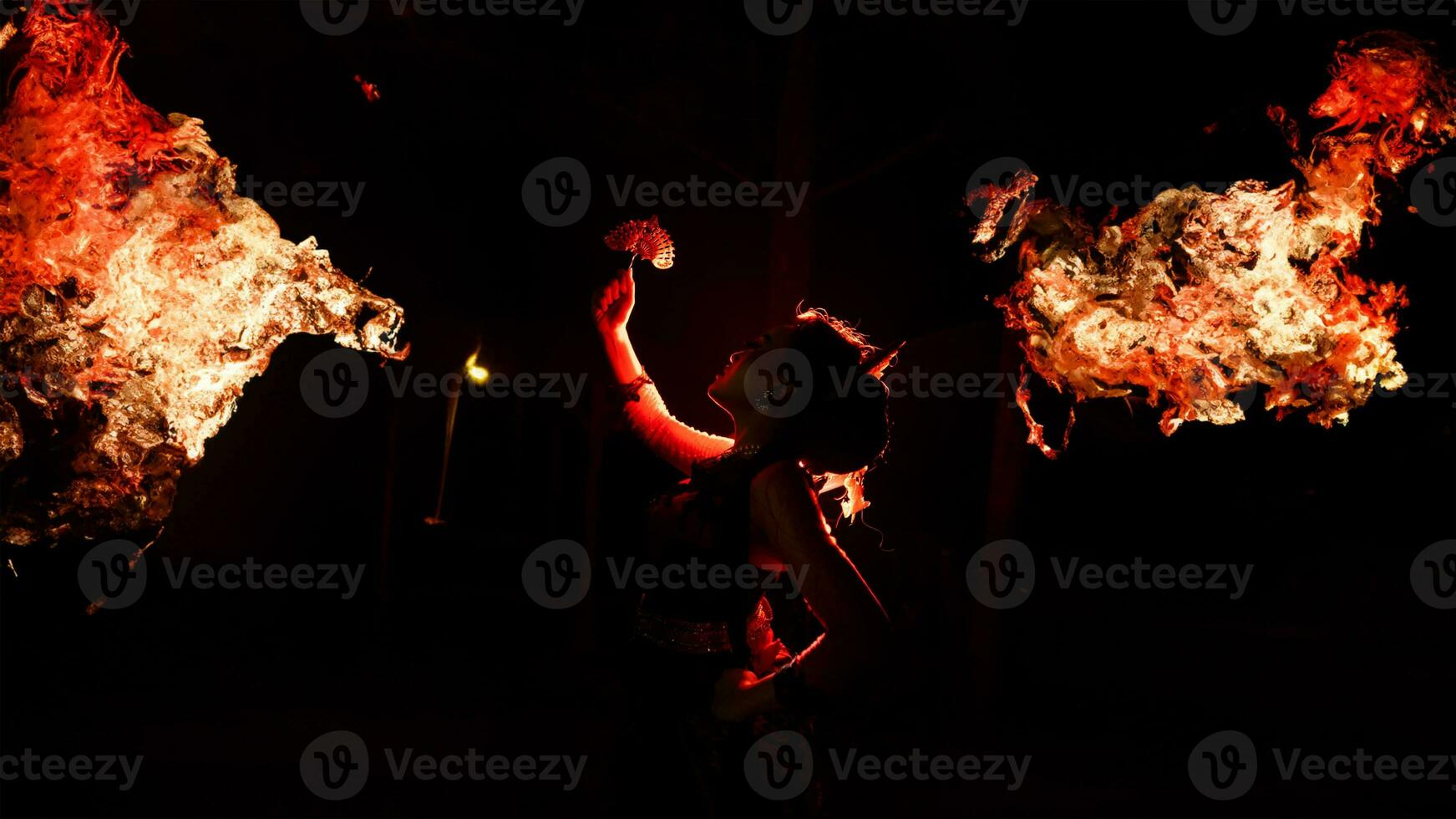 the silhouette of a female dancer holding jewelry shines brightly around the flames and looks bold in the dark photo