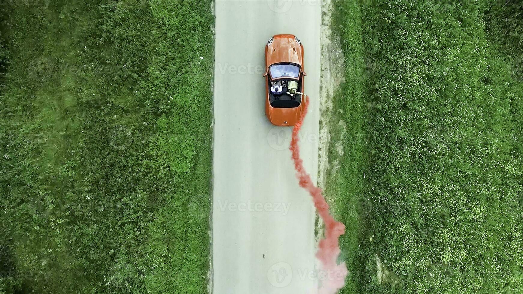 Aerial survey of red cabrioled goes on the road and couple using colored smoke.Flying over classic red convertible car traveling in the countryside at sunset with colored smoke. Lovers in the car photo