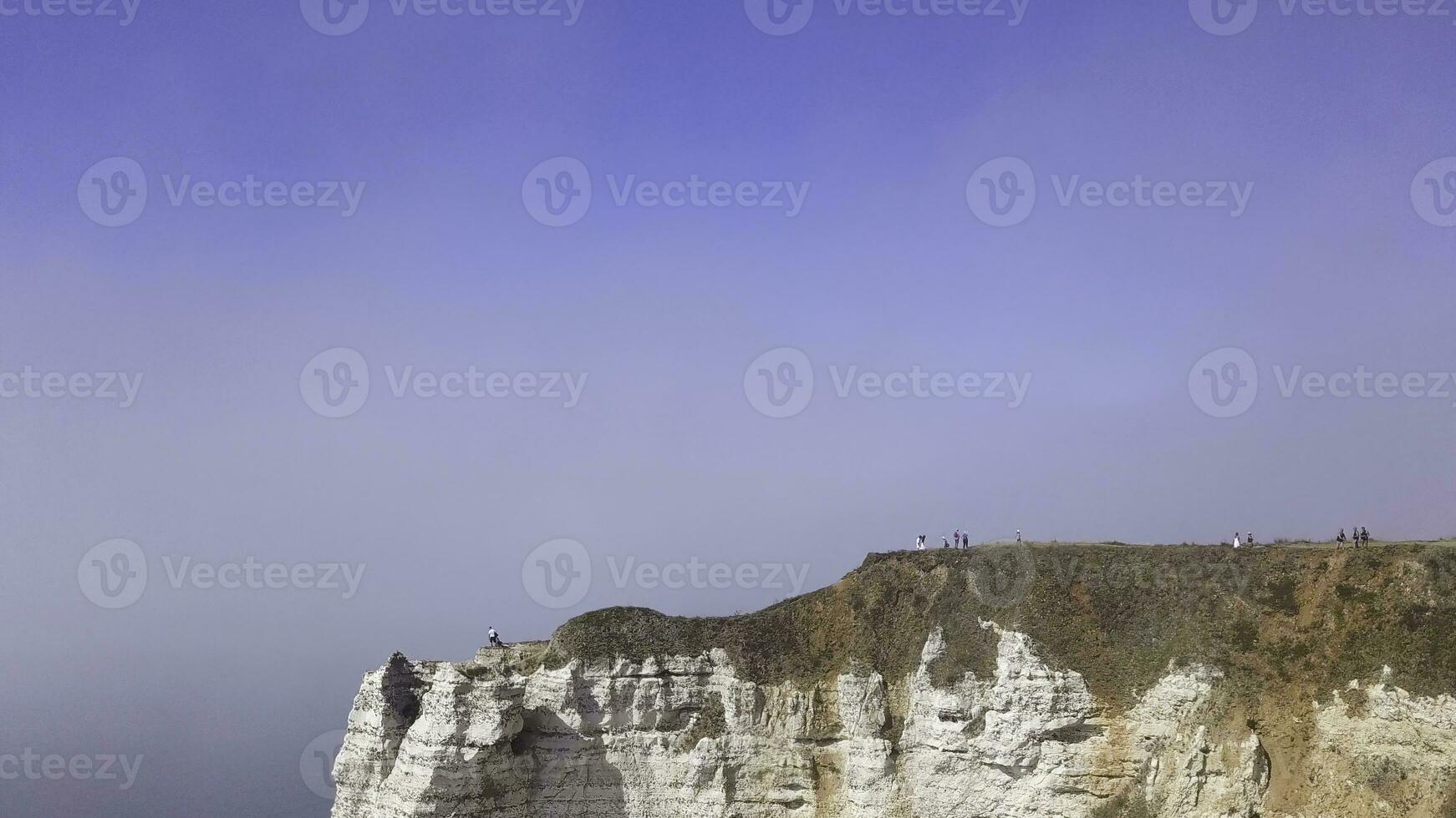 Aerial view of a beautiful white cliff on cloudy blue sky background, travel attraction. Action. Giant steep rock above the calm sea with people walking on its top. photo
