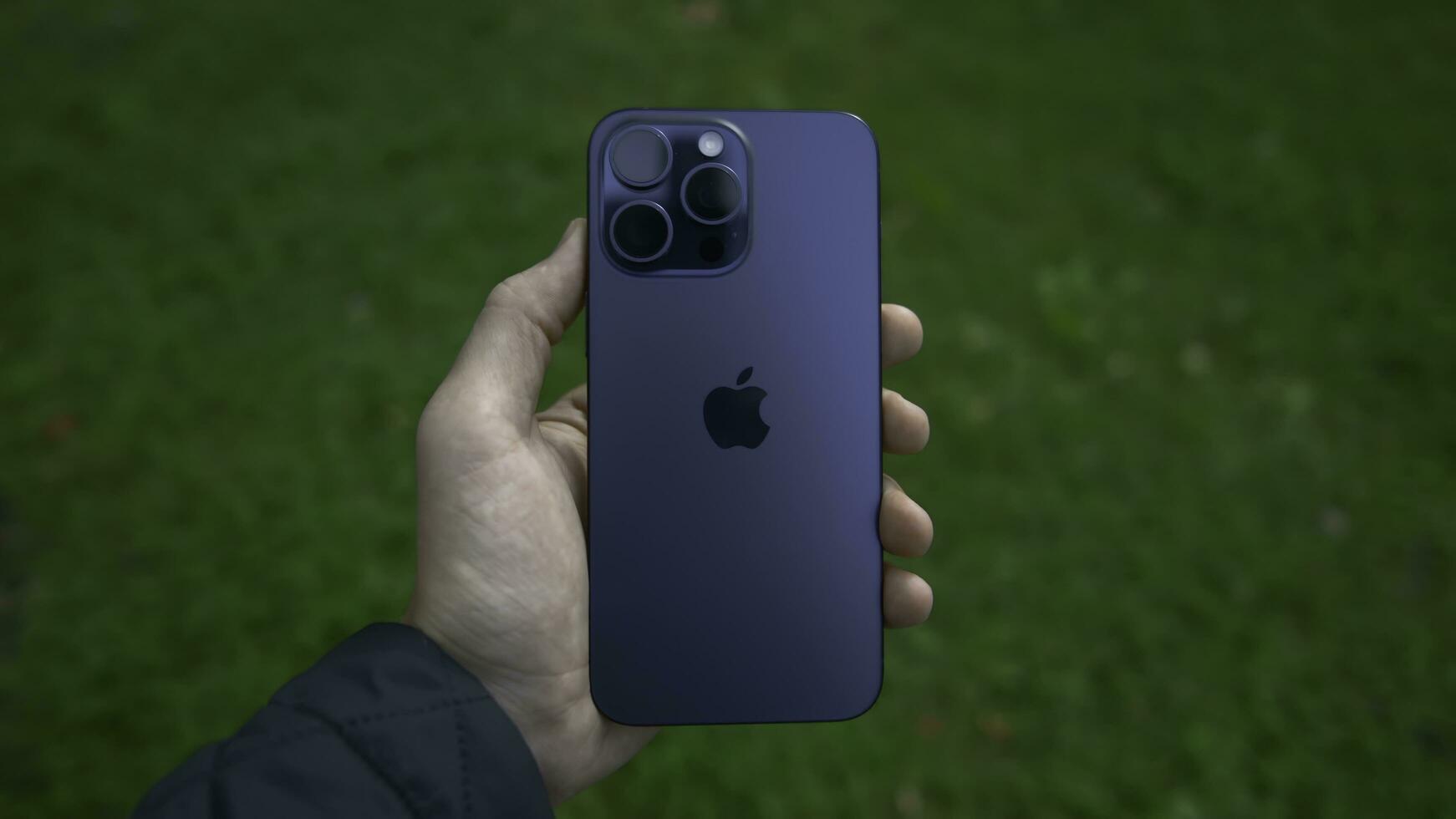China, Beijing - September 15, 2023. New iPhone model 15 pro. Action. Hand holds new model of stylish iPhone 15 pro. Man holds new iPhone 15 pro on background of green grass photo