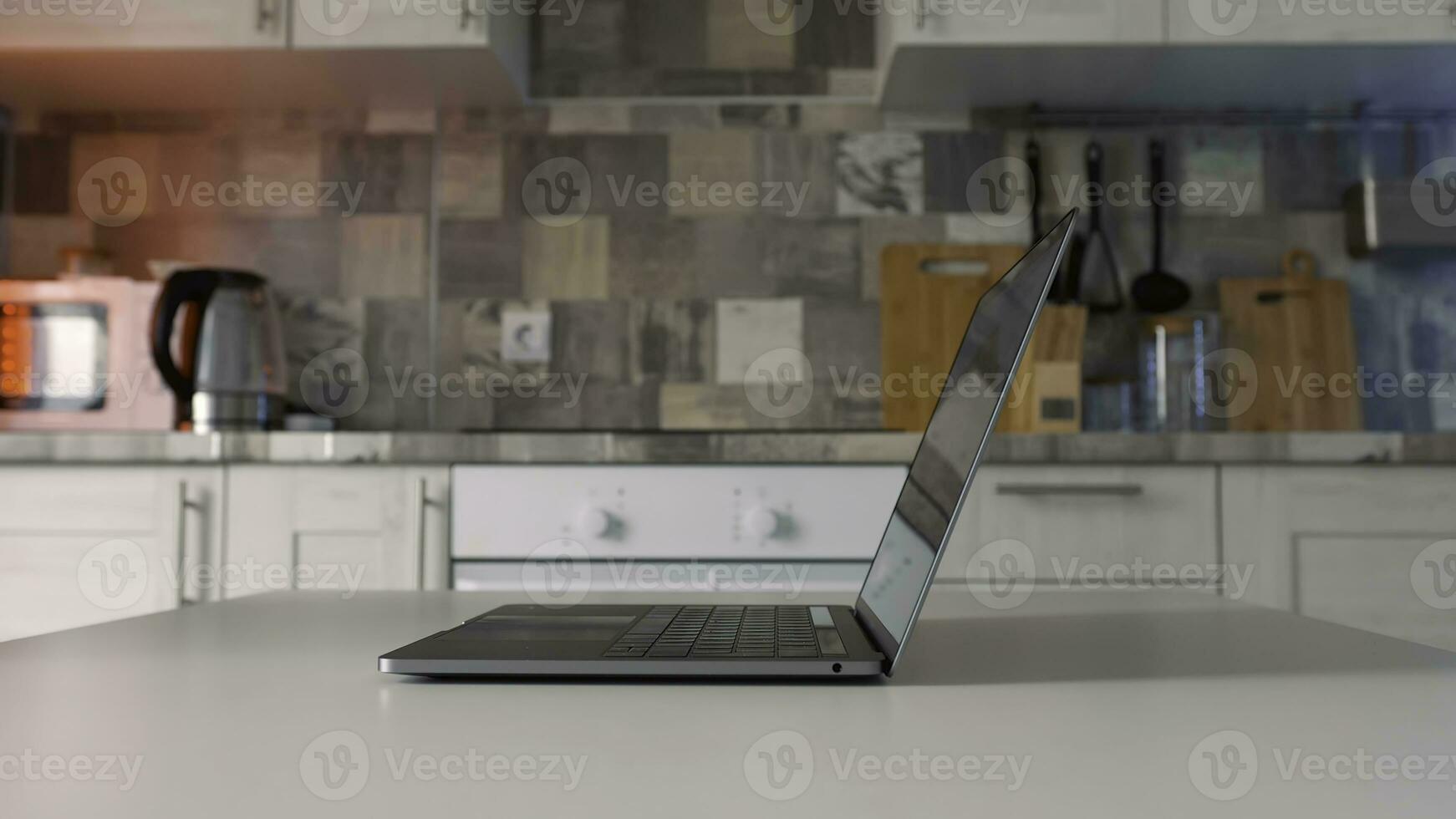 Concept of working at home during isolation. Action. Side view of male hands openning new silver laptop that is standing on the white table in the kitchen. photo