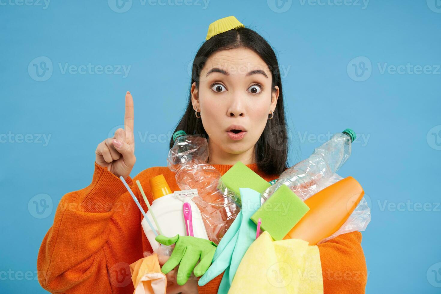 contento joven mujer señalando arriba, participación el plastico vacío botellas y basura para reciclaje, demostración eco bandera, clasificación estación anuncio publicitario, azul antecedentes foto