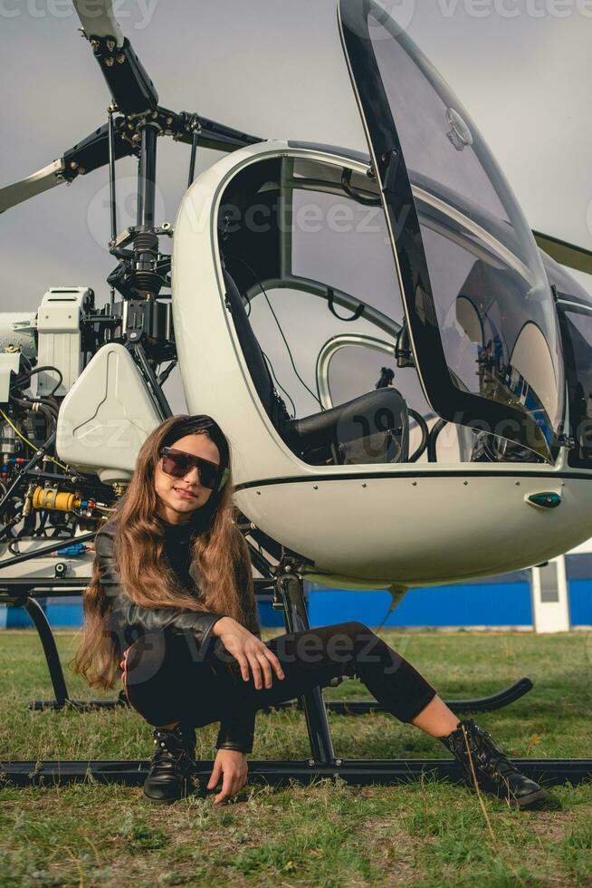 Smiling tween girl sitting near open helicopter on flying field photo