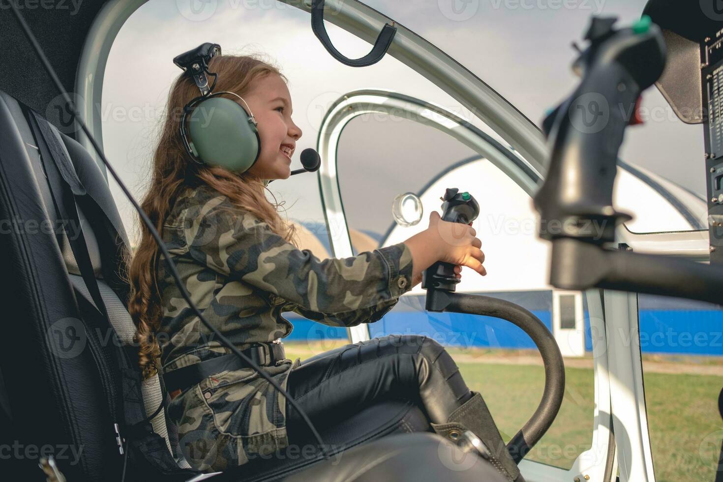 Smiling tween girl in aviator headset sitting in helicopter cockpit photo
