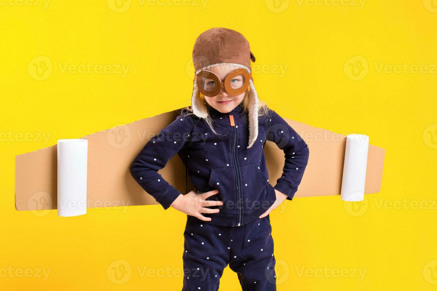 Freedom, girl playing to be airplane pilot, funny little girl with aviator cap and glasses, carries wings made of brown cardboard as an airplane photo