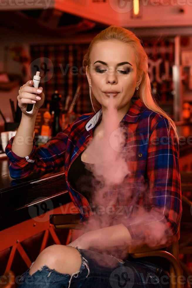 Young pretty woman smoke an electronic cigarette at the vape bar photo
