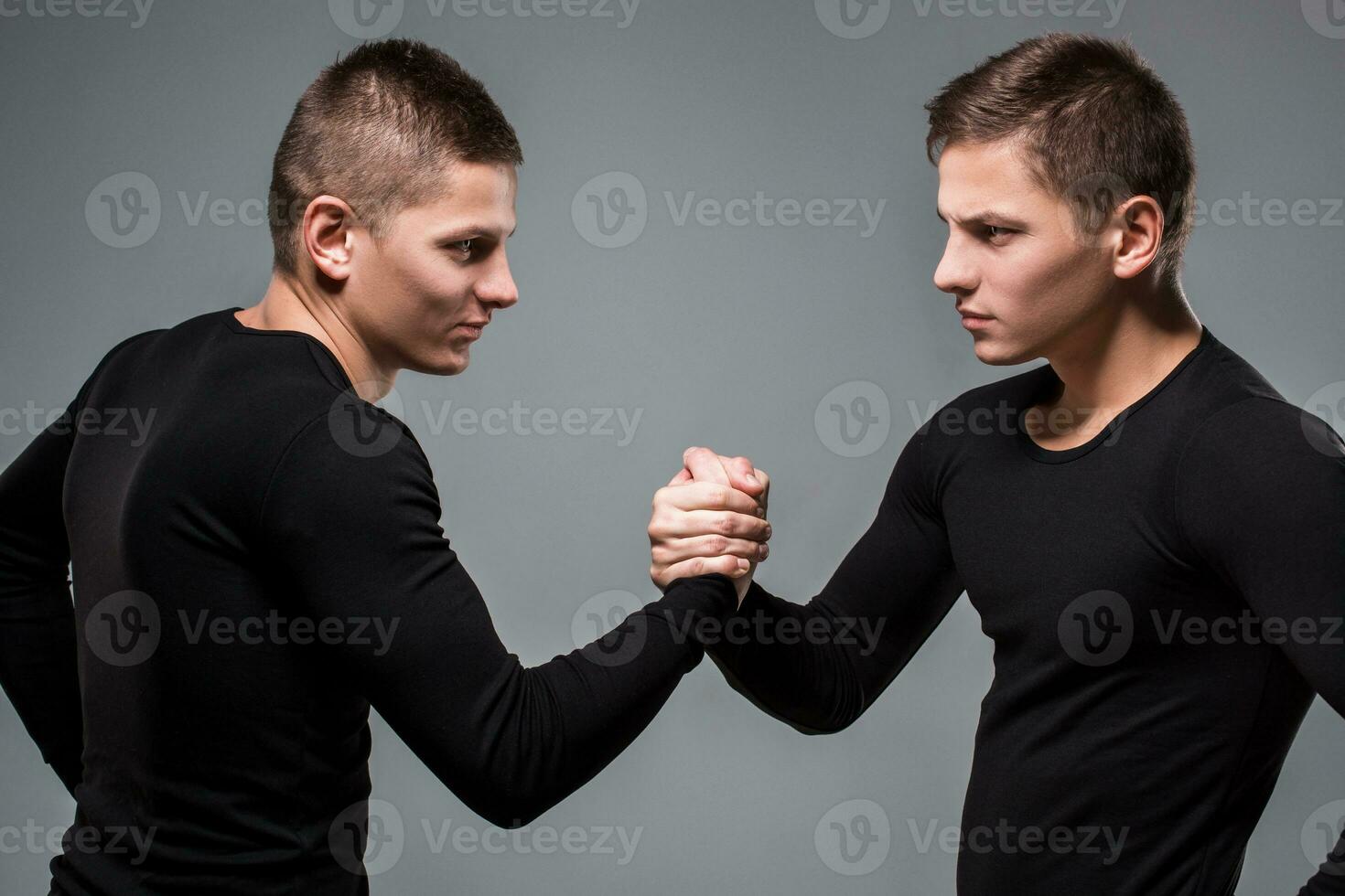 Portrait of young twin brothers standing face to face on gray ba photo