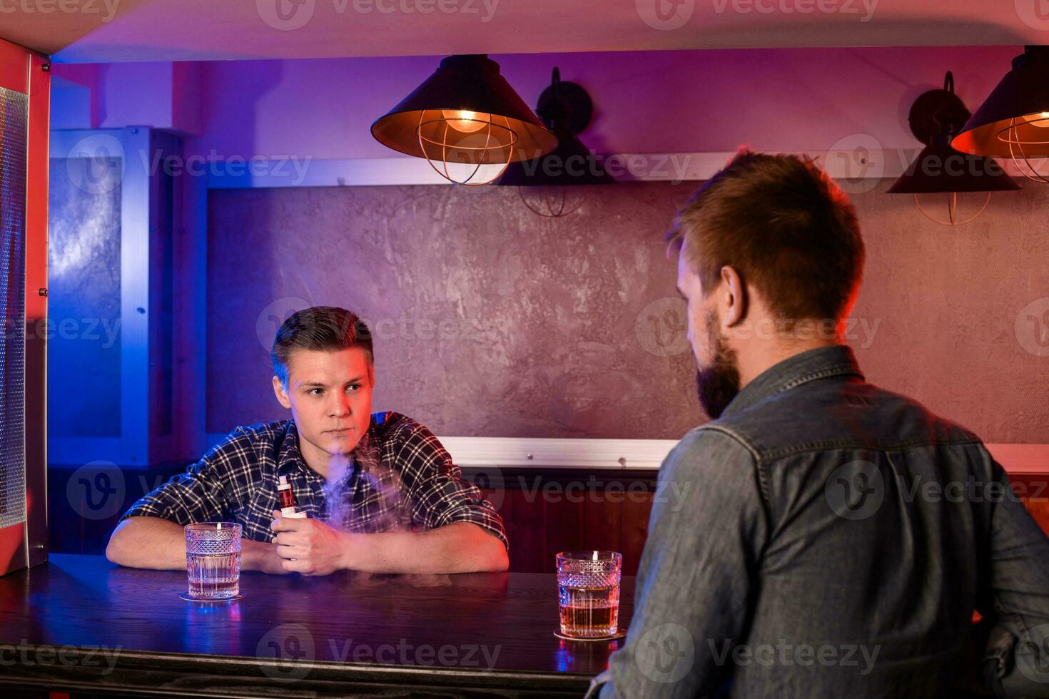 Two young men smoke electronic cigarettes in a vapebar photo