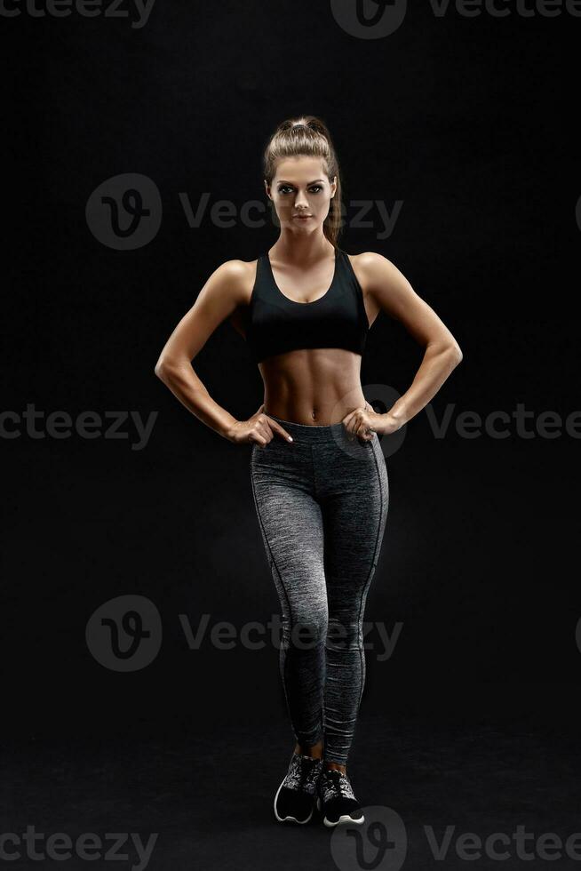 Shot of a strong woman with muscular abdomen in sportswear. Fitness female model posing on black background. photo