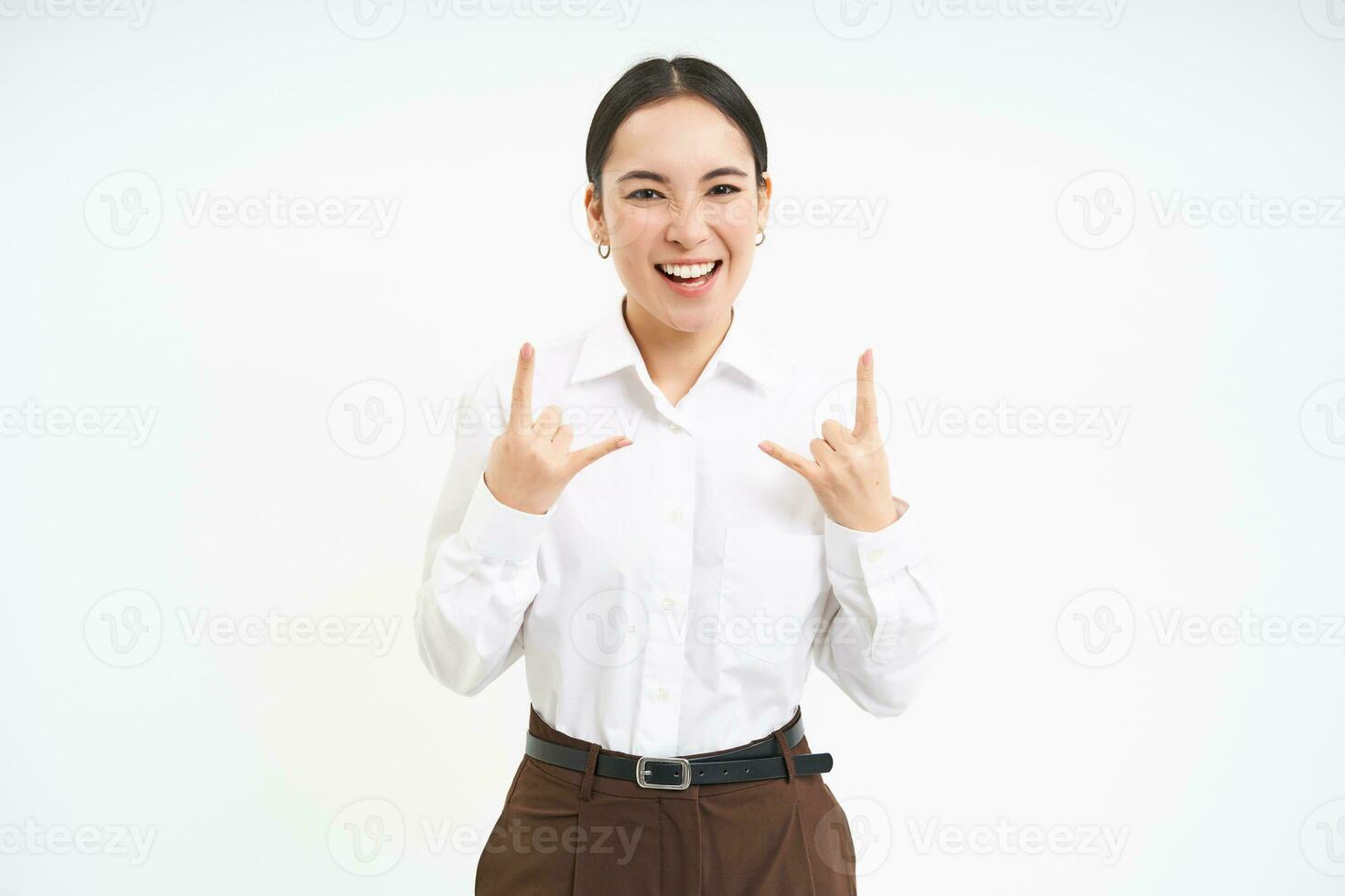 Excited smiling businesswoman, asian female employee, has fun, shows heavy metal, rock n roll gesture, celebrates, white background photo