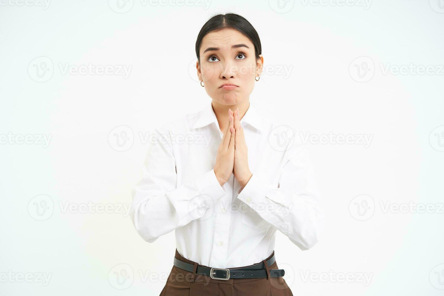 Hopeful corporate woman holds hand in pray, makes wish, looks up with hopeful face, standing over white background photo