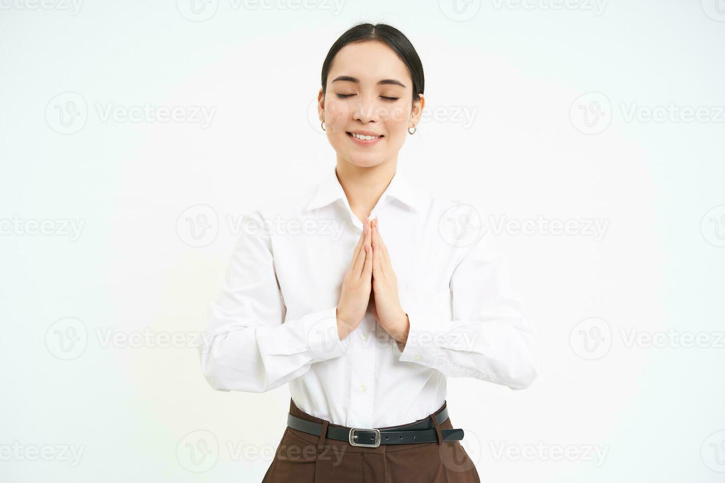 Smiling calm young woman, holds hands in pray with eyes closed, makes wish, hopes for smth, white background photo