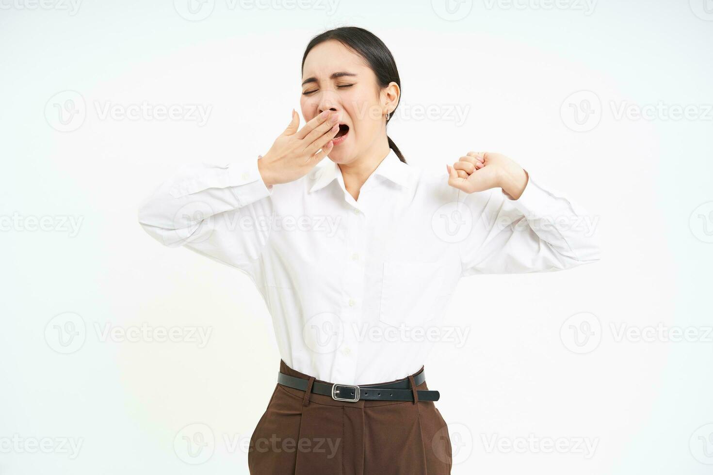 Tired asian corporate woman, yawns and stretches her back from fatigue after work, isolated on white background photo