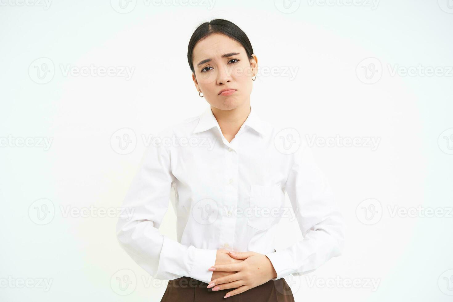 Image of asian office lady touches her belly, looks upset from discomfort in stomach, suffers period cramps at work, white background photo