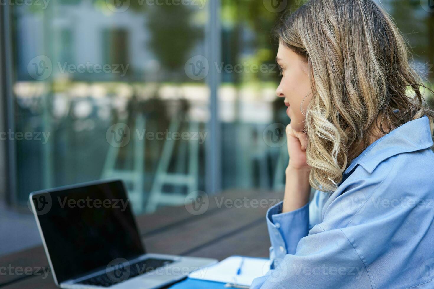 Close up portrait of woman student attend online course classes, sitting outside on fresh air with laptop and taking notes. Businesswoman video chat on computer photo