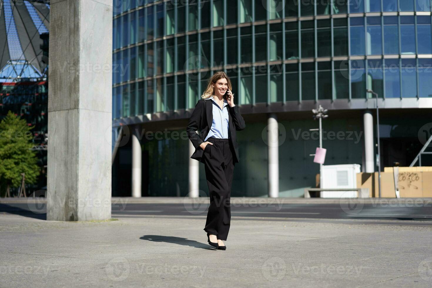 joven corporativo mujer en traje caminando en calle y hablando en móvil teléfono. mujer de negocios teniendo teléfono conversacion mientras yendo a trabajo foto