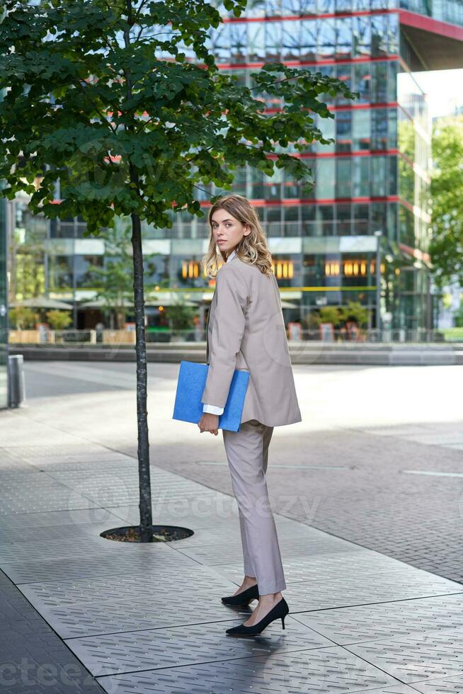 Portrait of businesswoman walking on street of an empty city center, holding folder with work documents photo