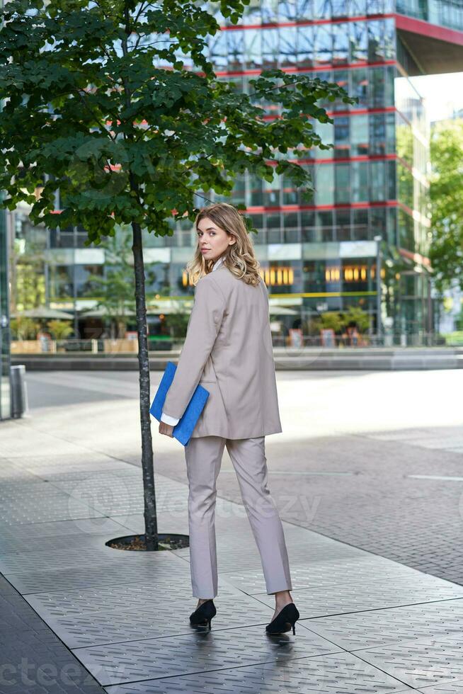 Portrait of businesswoman walking on street of an empty city center, holding folder with work documents photo
