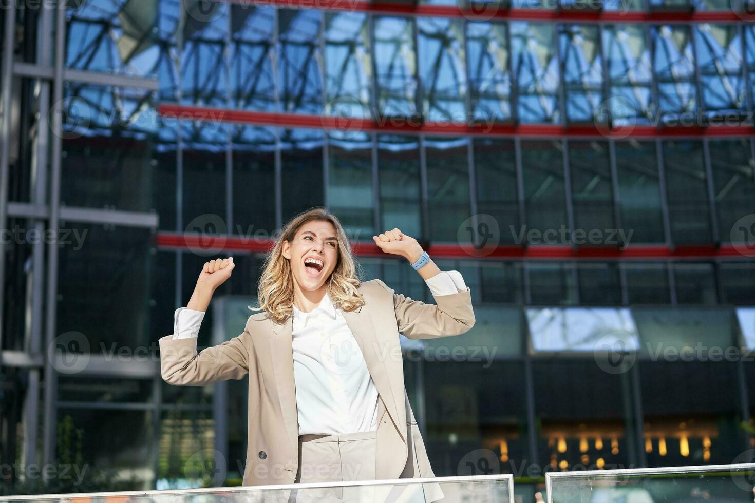 Happy businesswoman dancing on street, raising hands up. Corporate woman celebrates her victory or success photo