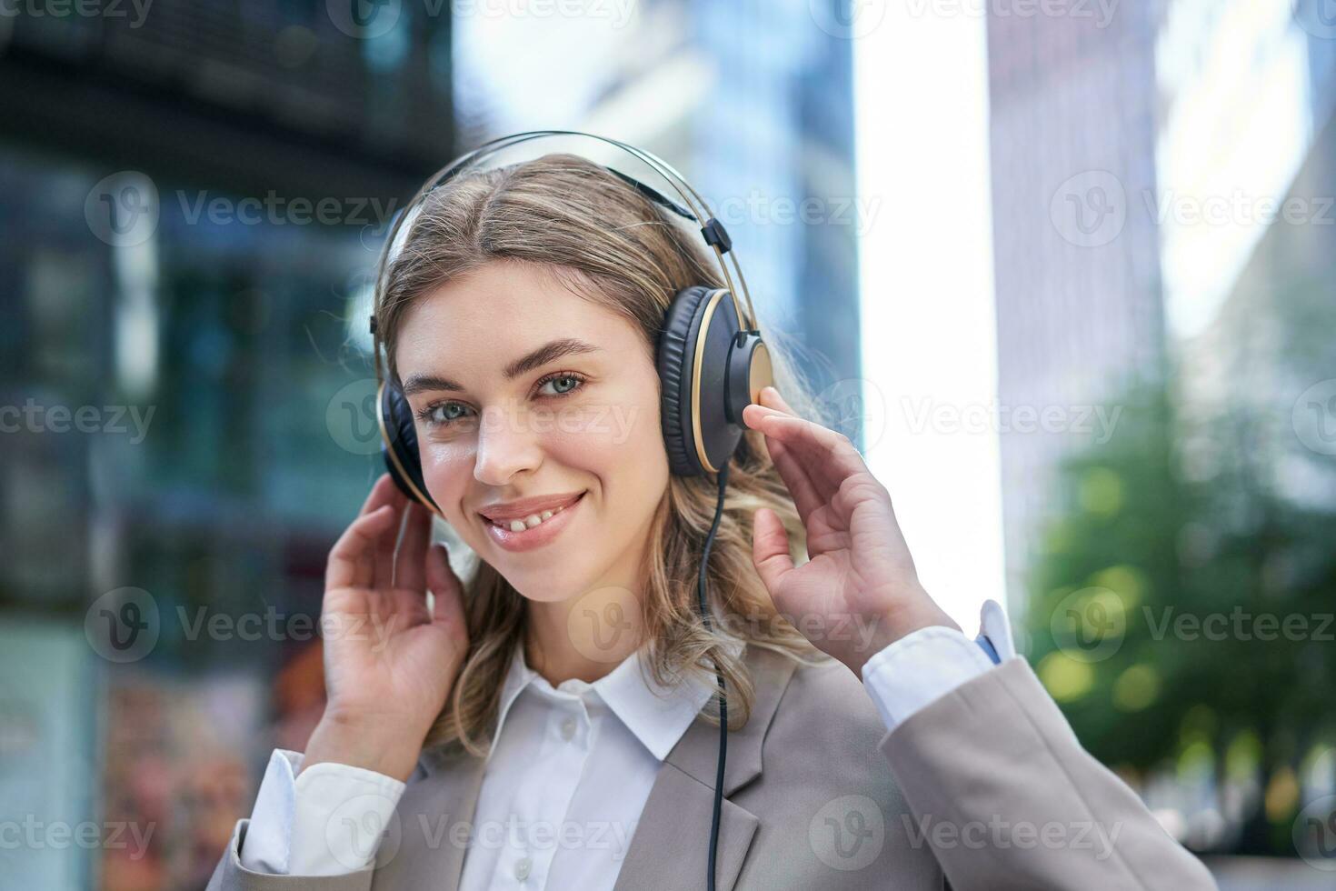 Happy woman listens to music in headphones while walking in city centre, smiling photo