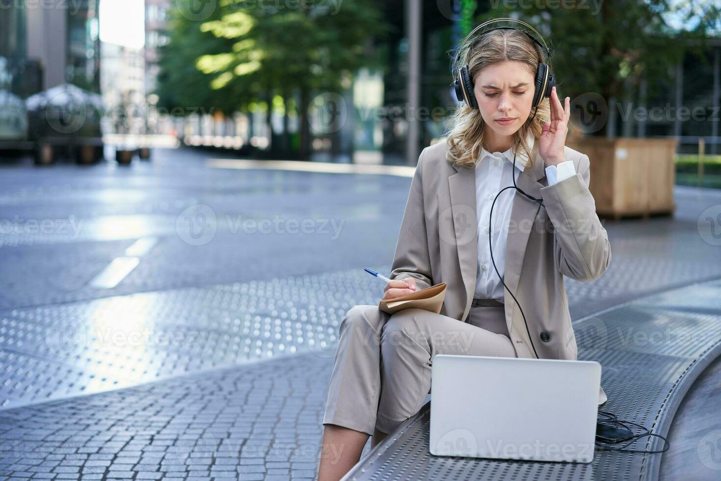 mujer de negocios mirando perplejo a computadora portátil, tomando notas en su computadora portátil, asistiendo en línea trabajo reunión mientras sentado en calle foto