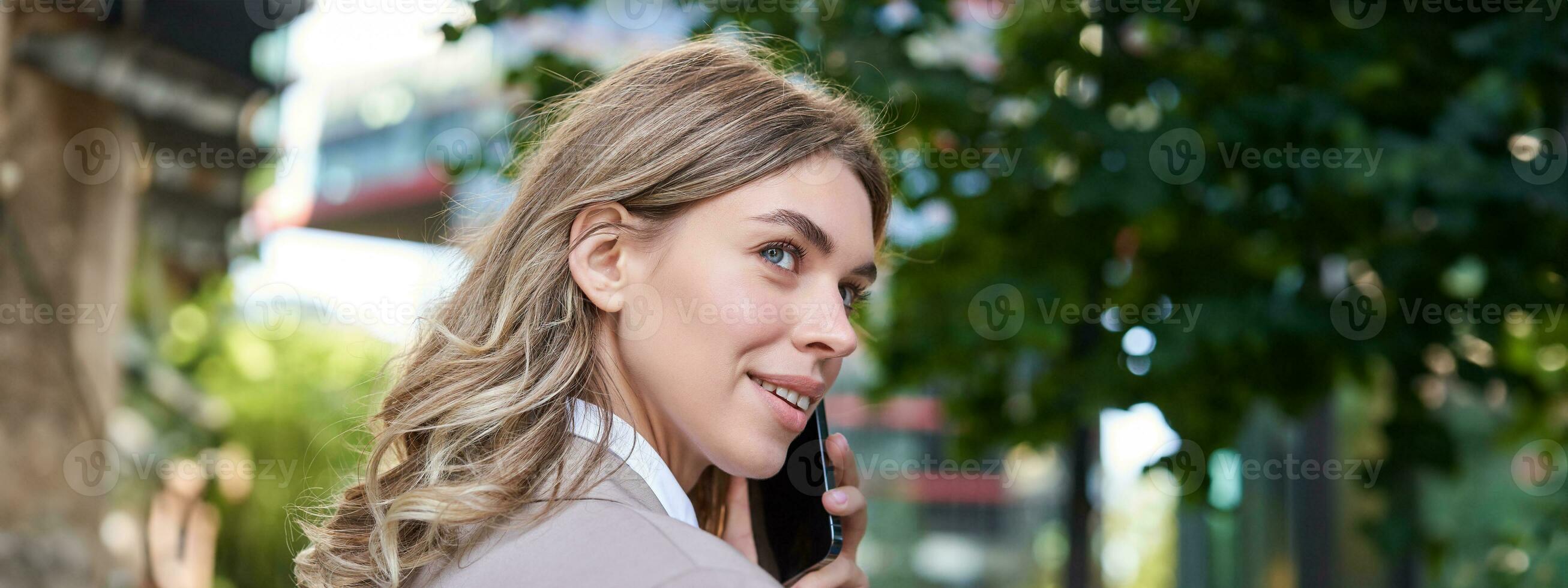 Close up portrait of corporate woman calling on mobile phone, walking on street with work documents in hand, wearing business suit photo