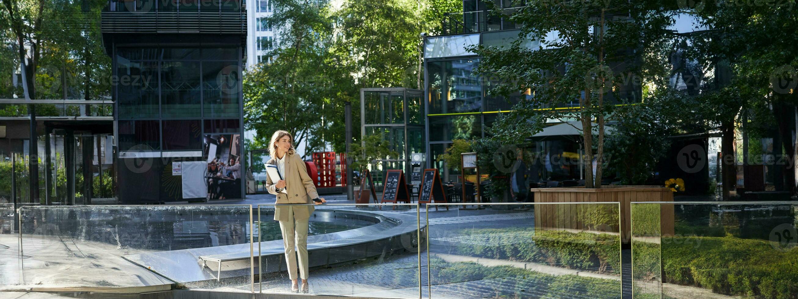 corporativo mujer en traje, en pie con confianza en beige traje con trabajando documentos al aire libre, posando en ciudad centrar foto