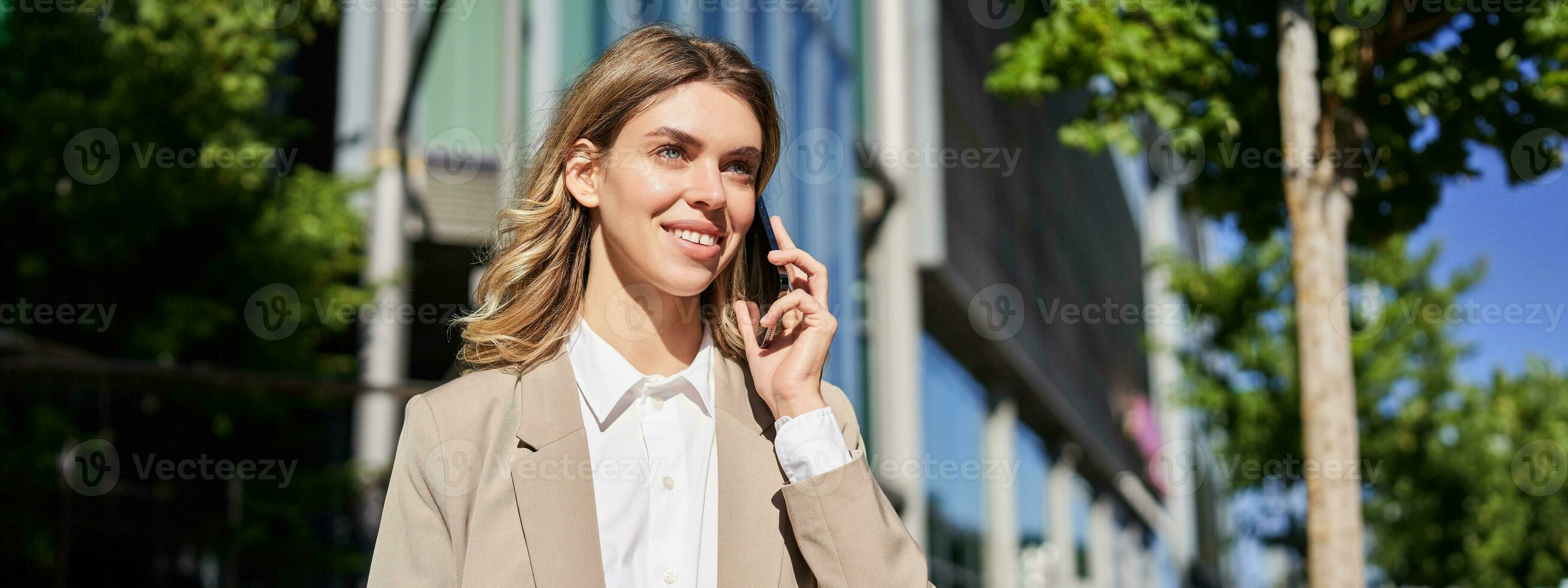 Portrait of businesswoman making a phone call, standing on street near office building, talking to someone on telephone photo