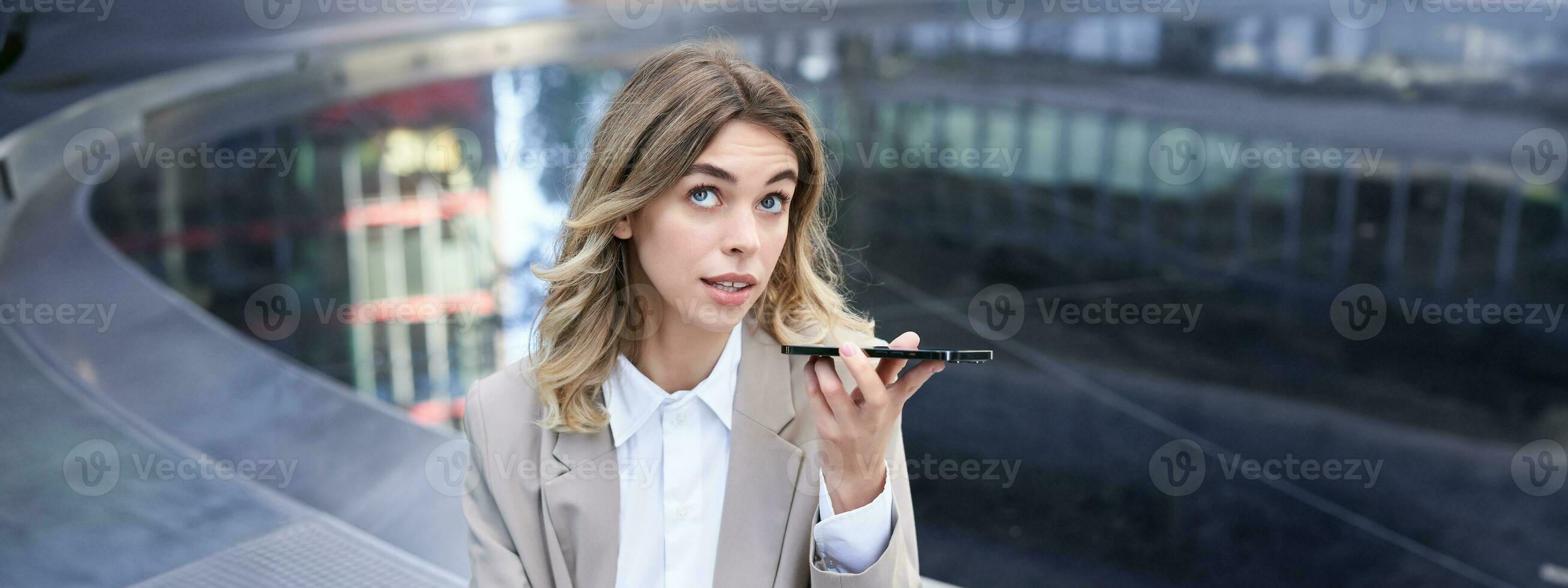 Young office girl talking on mobile phone, recording voice message, holding smartphone near mouth photo