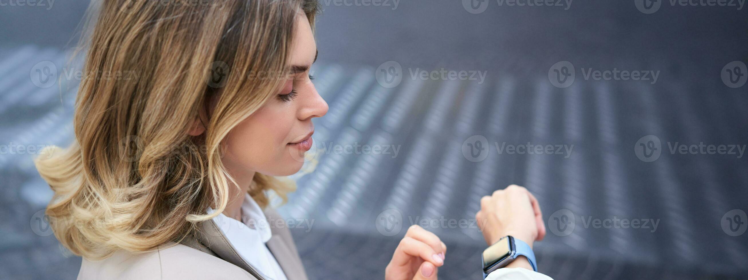 Close up portrait of business woman looking at her wrist digital watch, reading message, using app, standing outdoors in city center photo