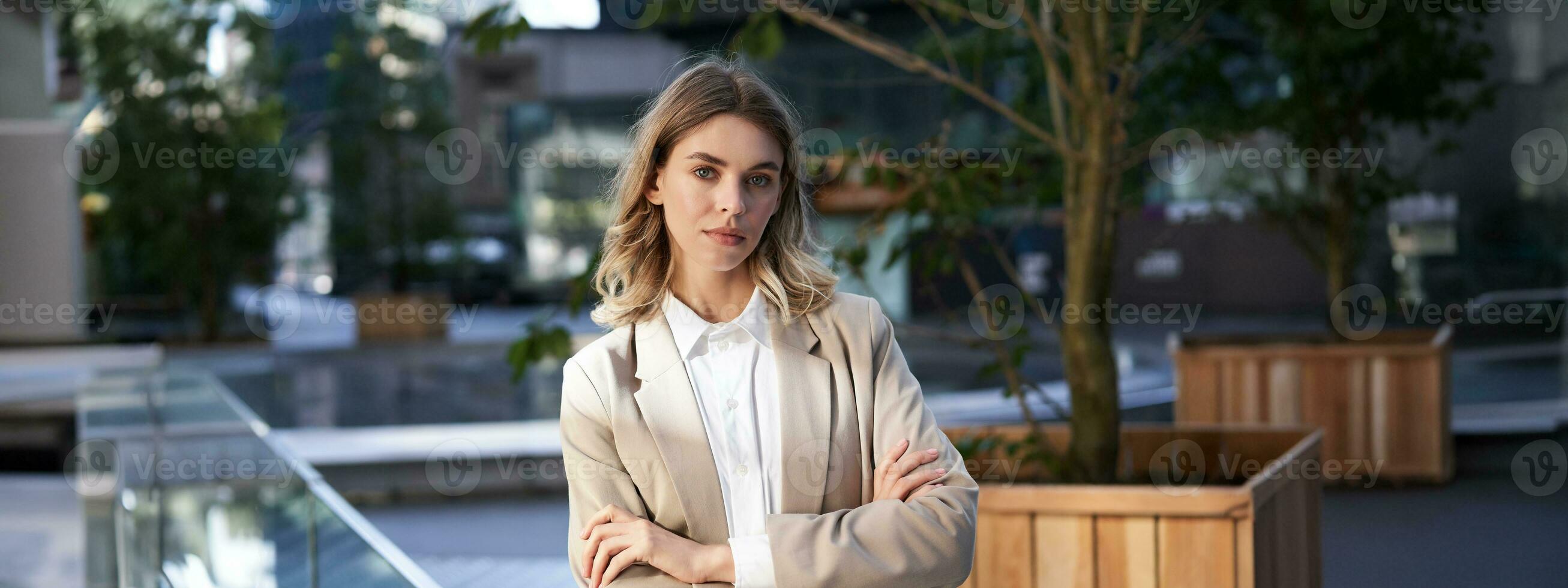 Close up portrait of confident and successful businesswoman in suit, cross arms on chest, standing in power pose on street near office building photo