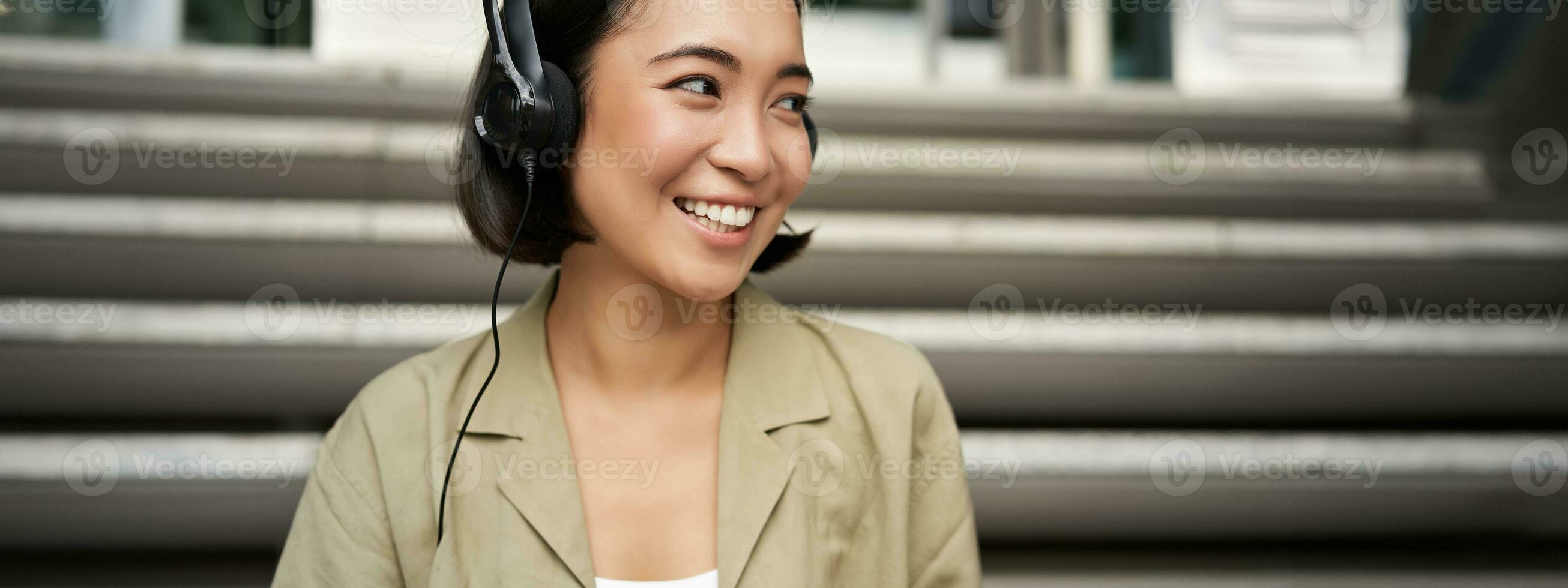 Portrait of beautiful girl in earphones, listening music, smiling and walking in city centre photo