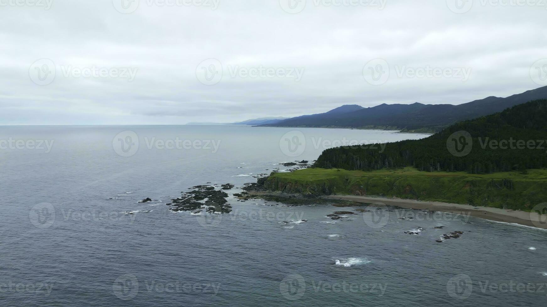 Green mountains with rocky reefs in cloudy weather. Clip. Landscape of mountain coast with green forest on cloudy day. Beautiful northern coast with green forest and blue sea waves photo