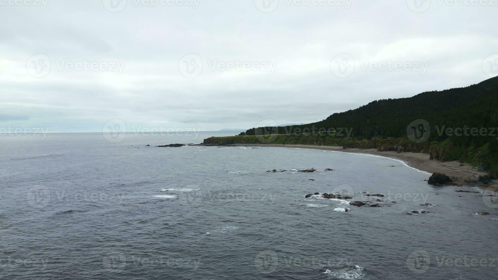 Green mountains with rocky reefs in cloudy weather. Clip. Landscape of mountain coast with green forest on cloudy day. Beautiful northern coast with green forest and blue sea waves photo