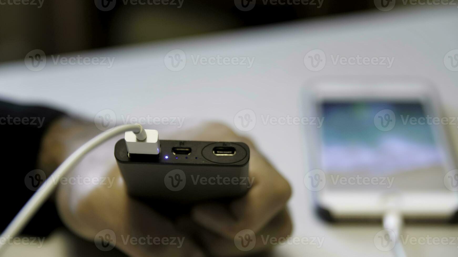 Black power bank and smartphone on a white table. Media. Close up of male hand inserting usb cable into portable power bank to charge cell phone device. photo