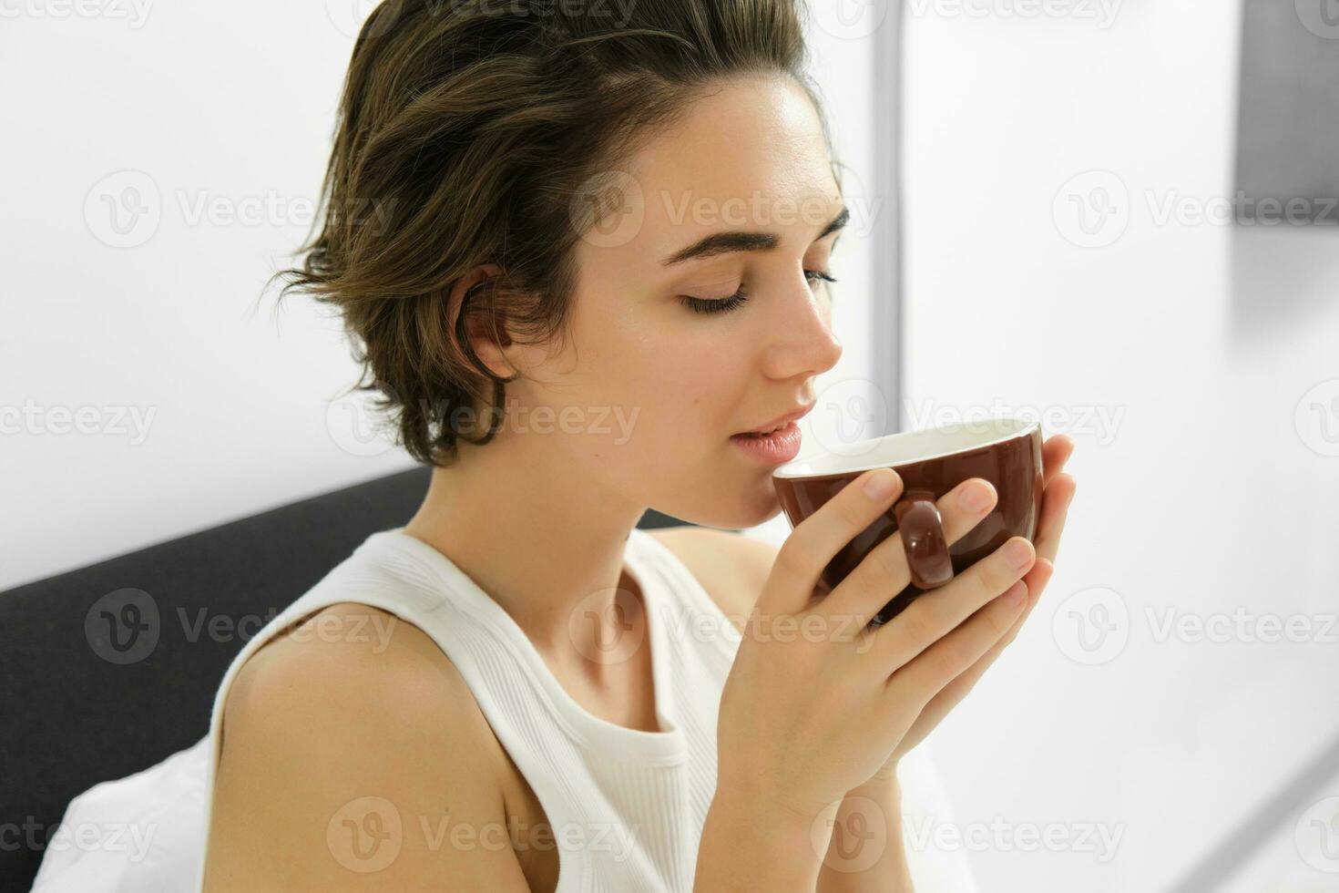 retrato de joven mujer despertar arriba, Bebiendo café en cama, oliendo favorito aroma foto