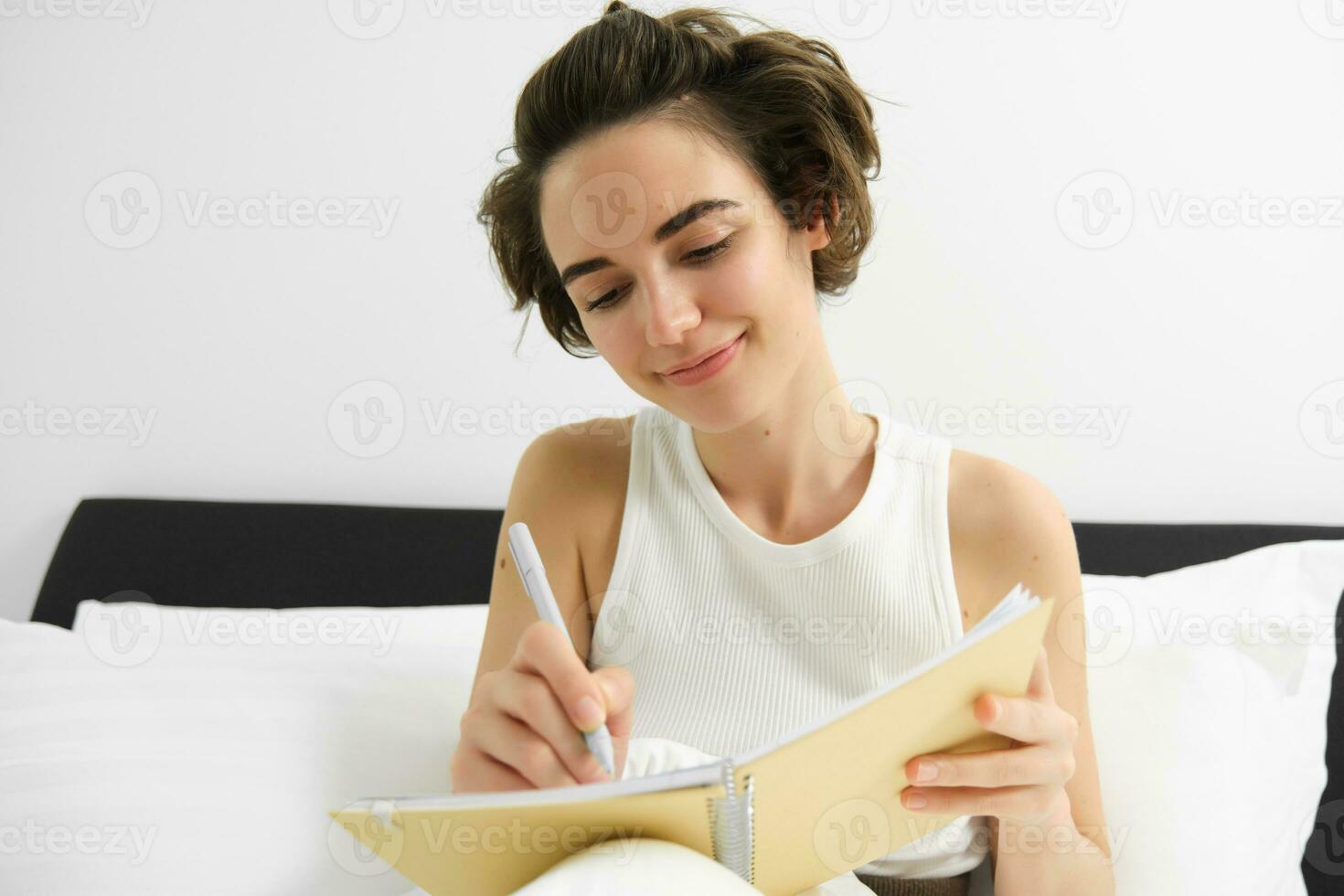 Portrait of woman sitting in bed with journal, writing in her 