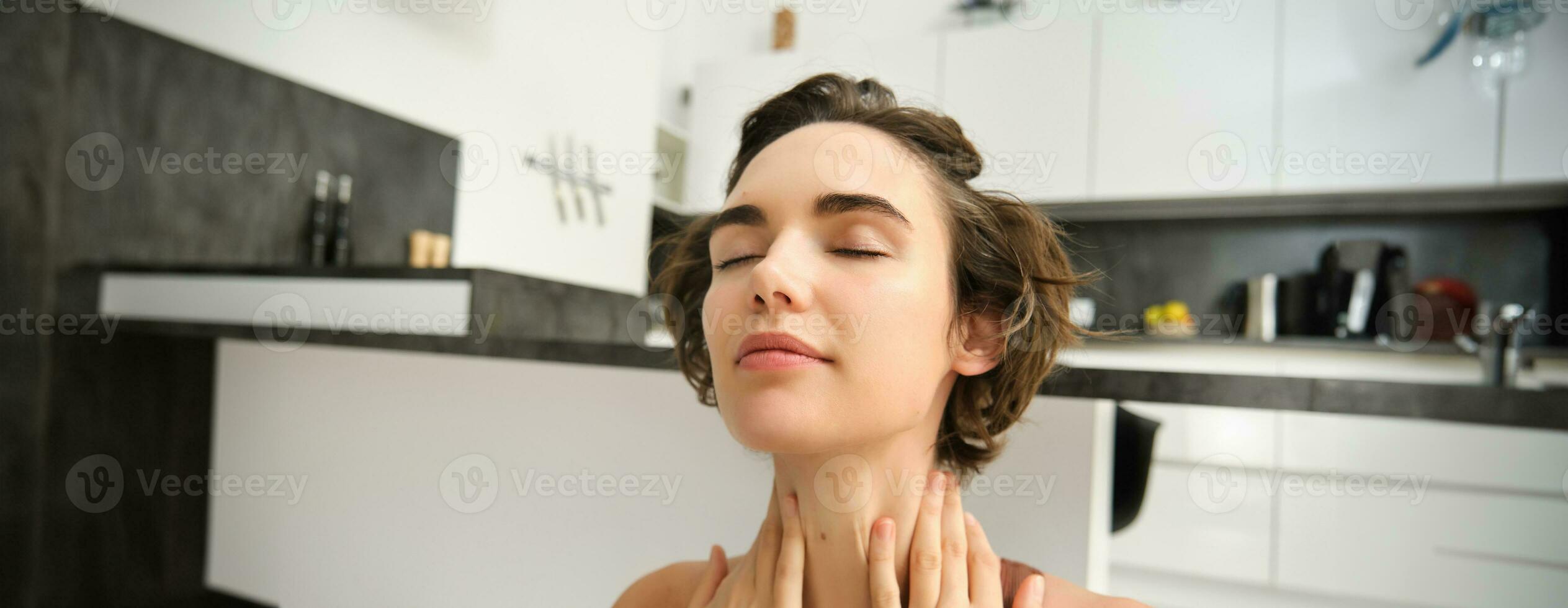 Close up portrait of sportswoman, fitness woman massaging her neck, warm-up her body after workout, doing yoga on rubber mat at home photo