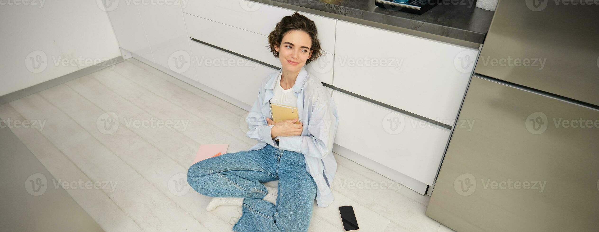 Superior ángulo Disparo de joven mujer sentado en cocina piso, revisando para examen, leyendo su notas, haciendo deberes a hogar foto