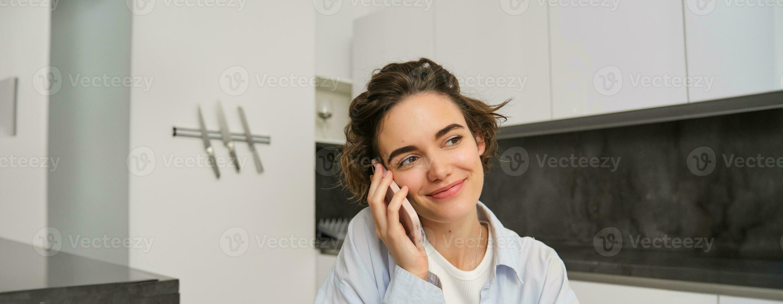 Image of woman working at home, making a phone call, sitting with smartphone, surrounded with paperwork, doing homework and talking to someone photo