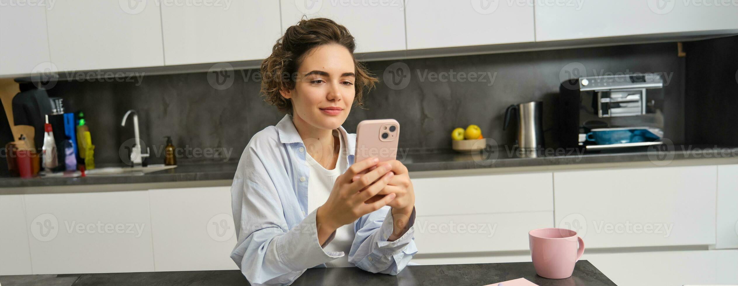 Portrait of beautiful smiling woman sitting at home with smartphone, using mobile phone app, orders groceries delivery photo