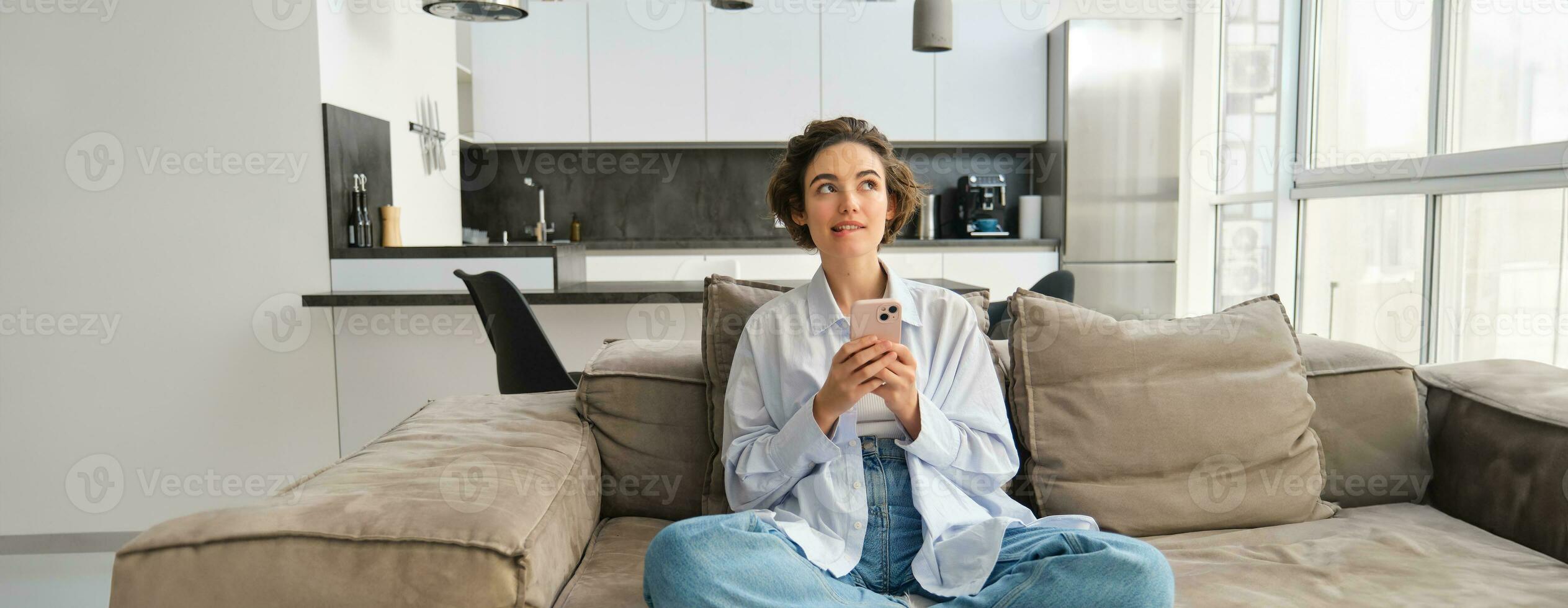 Portrait of smiling woman chats on smartphone app, sits at home on sofa and uses mobile phone application photo