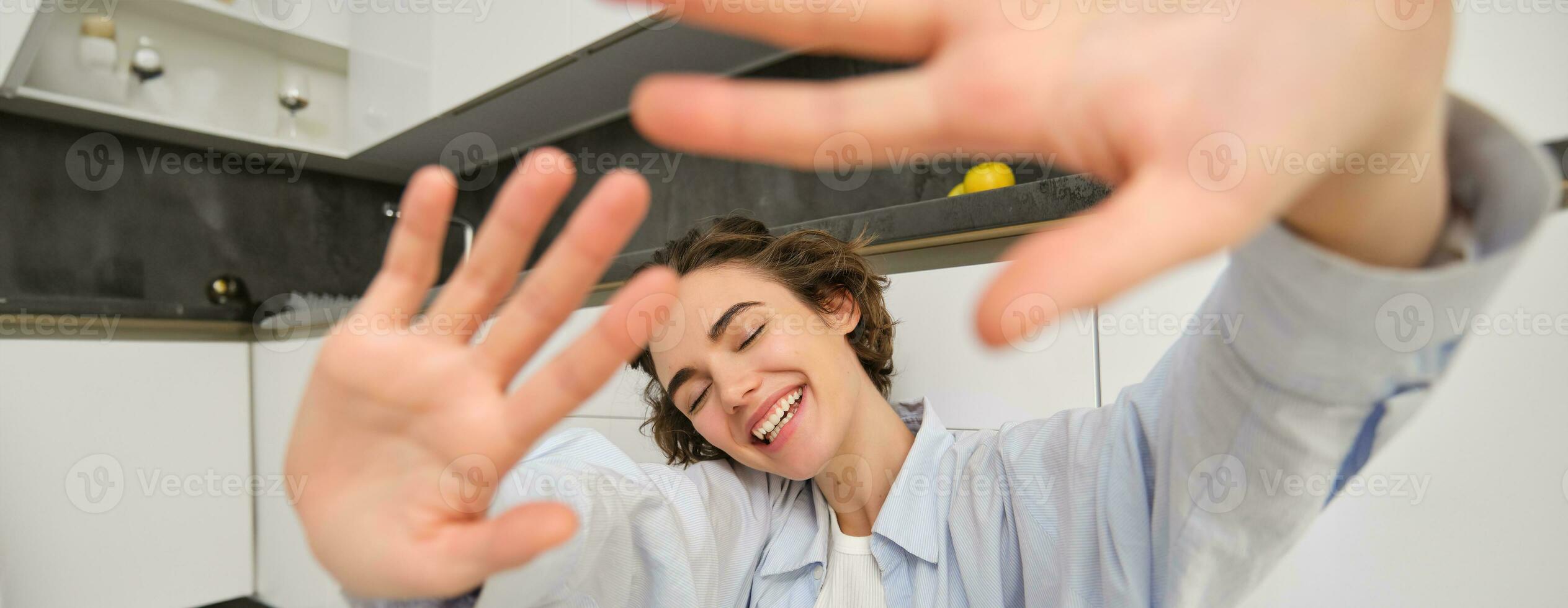 Lifestyle and people concept. Young happy woman hides from camera, extends hands forward, laughs and smiles carefree, spends time at home with joy photo