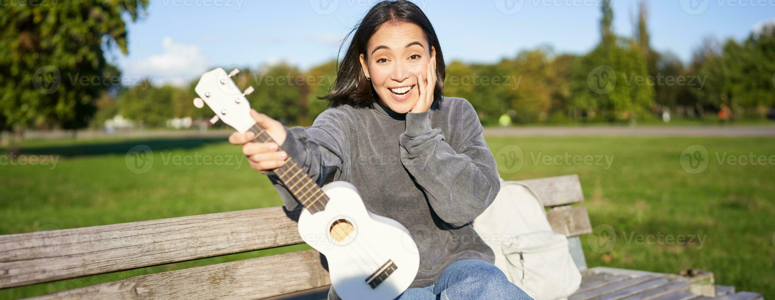 retrato de joven niña músico, sentado en parque con ukelele guitarra, mirando sorprendido a cámara, diciendo Guau foto